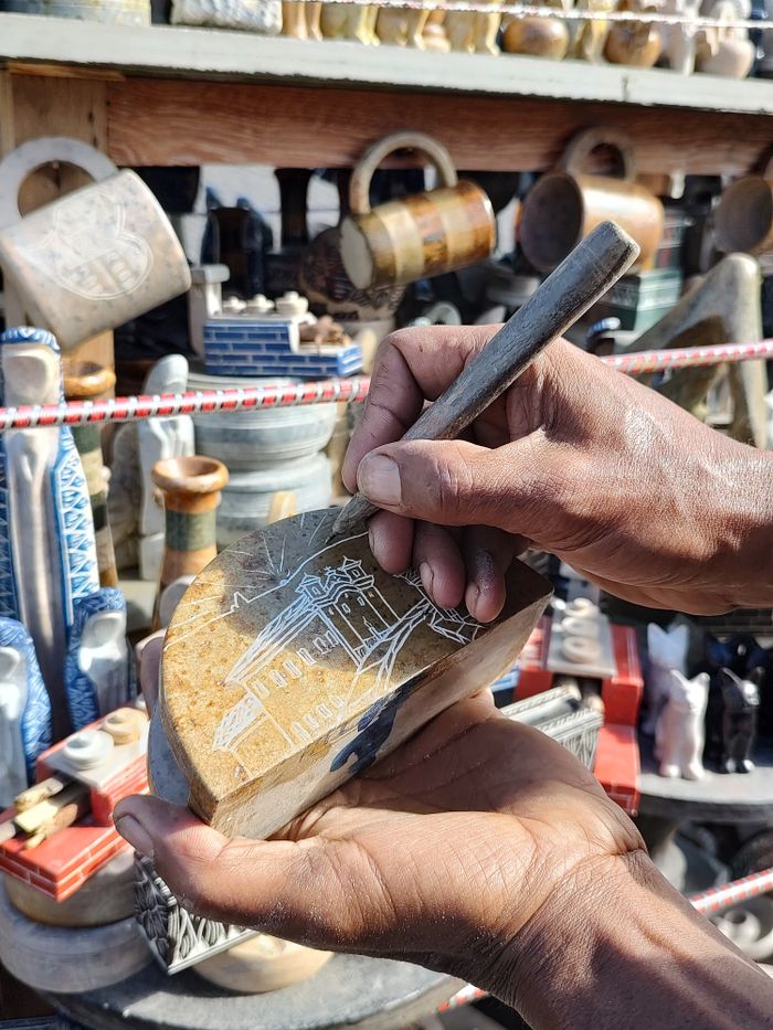 Close-up of an artisan engraving a wooden shoe in a vibrant craft market setting.